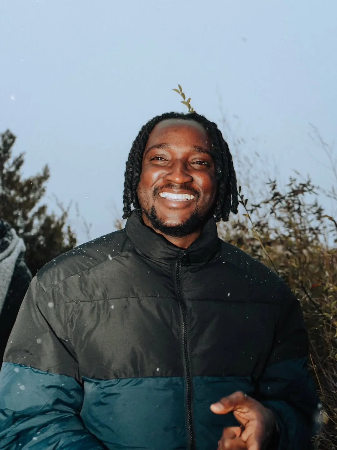 Portrait d’Ange N’Guessan, souriant, en doudoune, à la tombée du jour